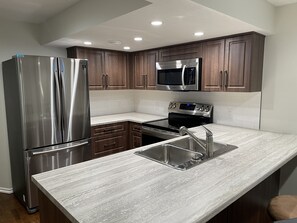 A modern kitchen with stainless steel appliances, a double sink, and wooden cabinets. - Beautiful, modern and accessible 2bdr BSMT suite with large backyard for kids (St. Albert)