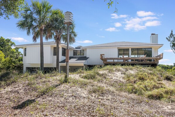 A modern house with a large deck, surrounded by natural vegetation and a clear sky. - Bald Head Island Beach House on golf course beach access #9 Sleeps up to 15 (Bald Head Island)