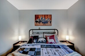 Une chambre à coucher comprenant un lit, deux tables de chevet, un tableau accroché au mur et un luminaire au plafond.