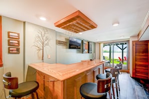 Une cuisine moderne avec un bar en bois, des tabourets de bar, une grande fenêtre et une vue sur l’extérieur.