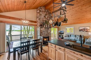 Una cocina amplia con chimenea de piedra, techo de madera y comedor con vistas al exterior.