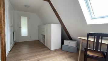 Een kamer met een schuine kap, houten balken, een witte garderobe, een tafeltje en een stoel.