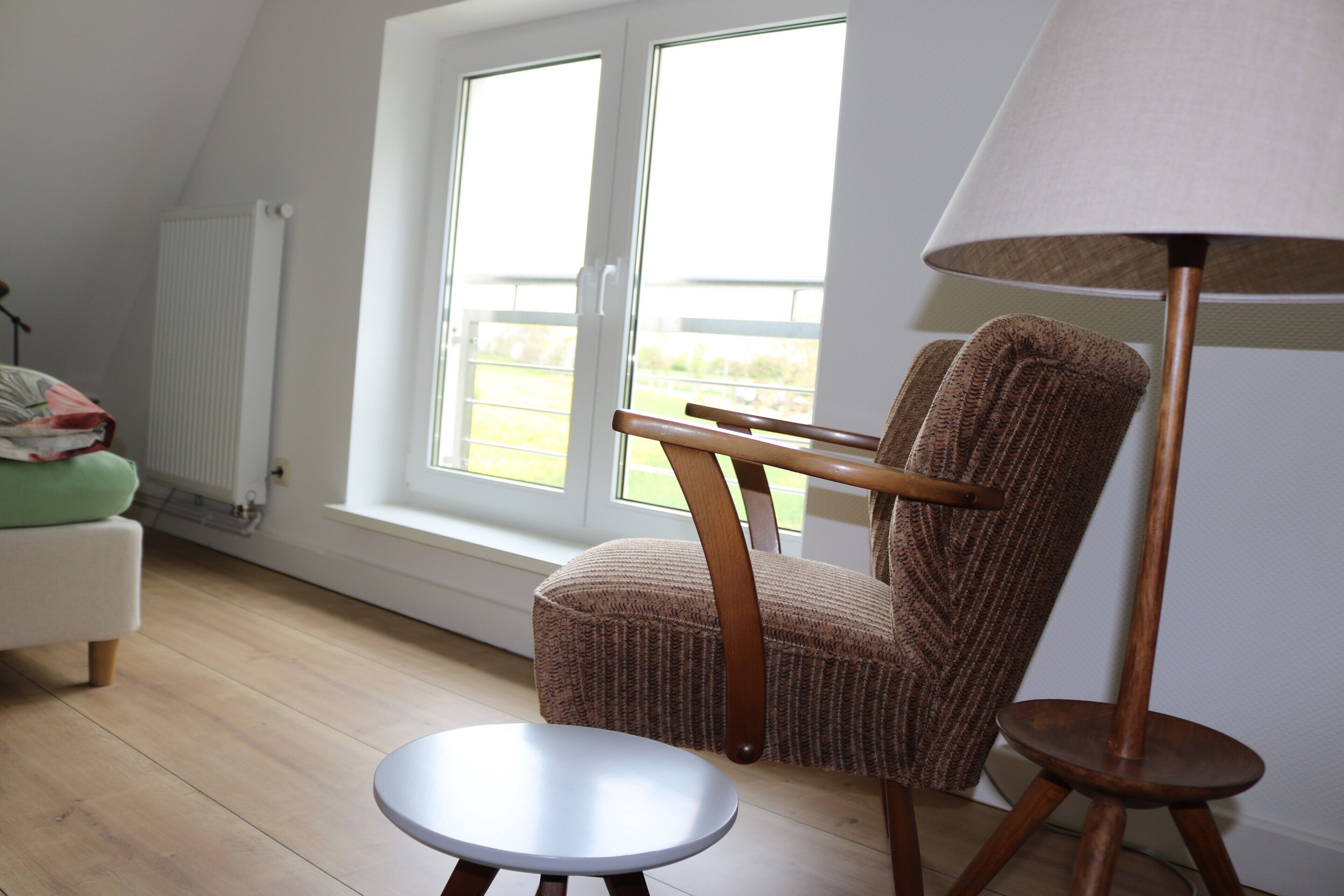 A room with a window, a chair, a small table, and a floor lamp.