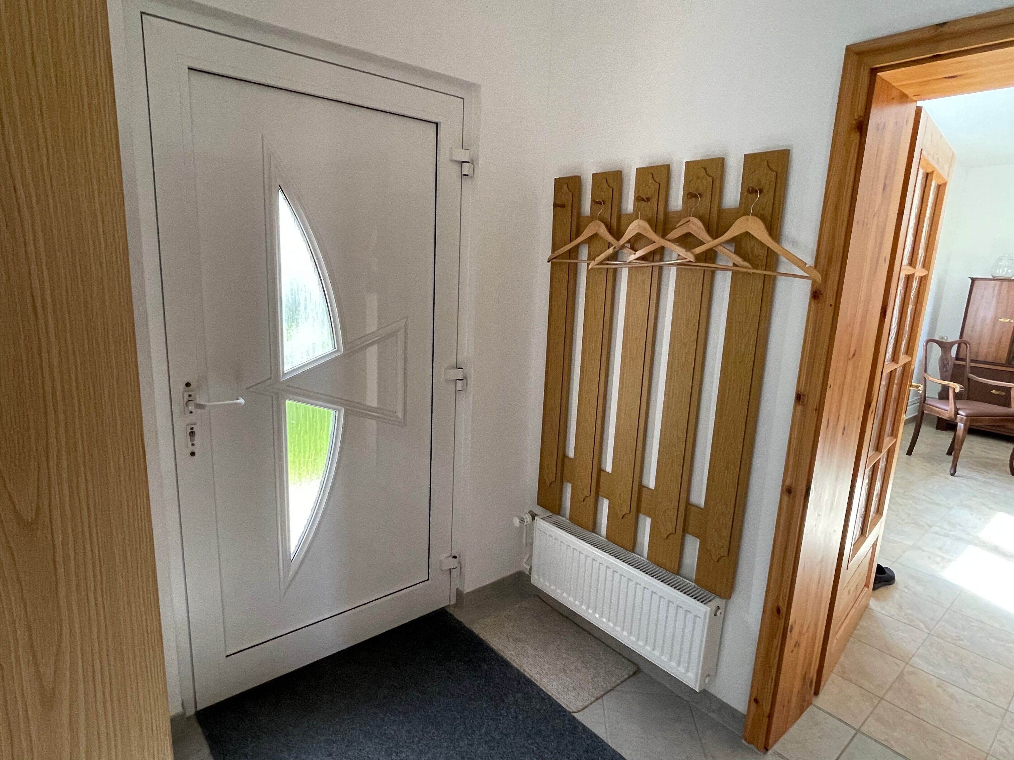Ein Zimmer mit einer weißen Tür, einem Heizkörper, einem hölzernen Kleiderständer und einem dunklen Teppich.