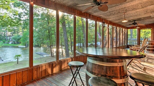 A rustic wooden interior with large windows overlooking a forested area and a body of water. - Lakefront cypress cabin (Florien)