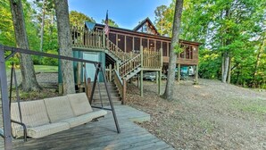 A cabin with a wooden deck, a swing set, and a staircase leading to a deck. - Lakefront cypress cabin (Florien)