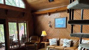 A cozy living room with a large window, leather furniture, and a wooden ceiling. - Lakefront cypress cabin (Florien)