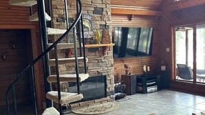 A spacious living room with a stone fireplace, a wooden staircase, a leather sofa, and a flat-screen TV mounted on the wall. - Lakefront cypress cabin (Florien)
