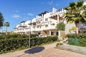 A multi-story hotel with balconies, a paved walkway, and lush greenery.