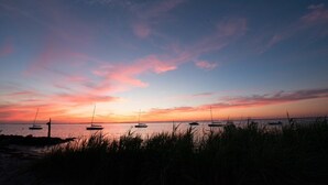 Una puesta de sol sobre una playa con veleros anclados en el agua.