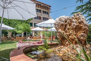 Un patio con mobiliario exterior, una formación rocosa y un pequeño elemento acuático.