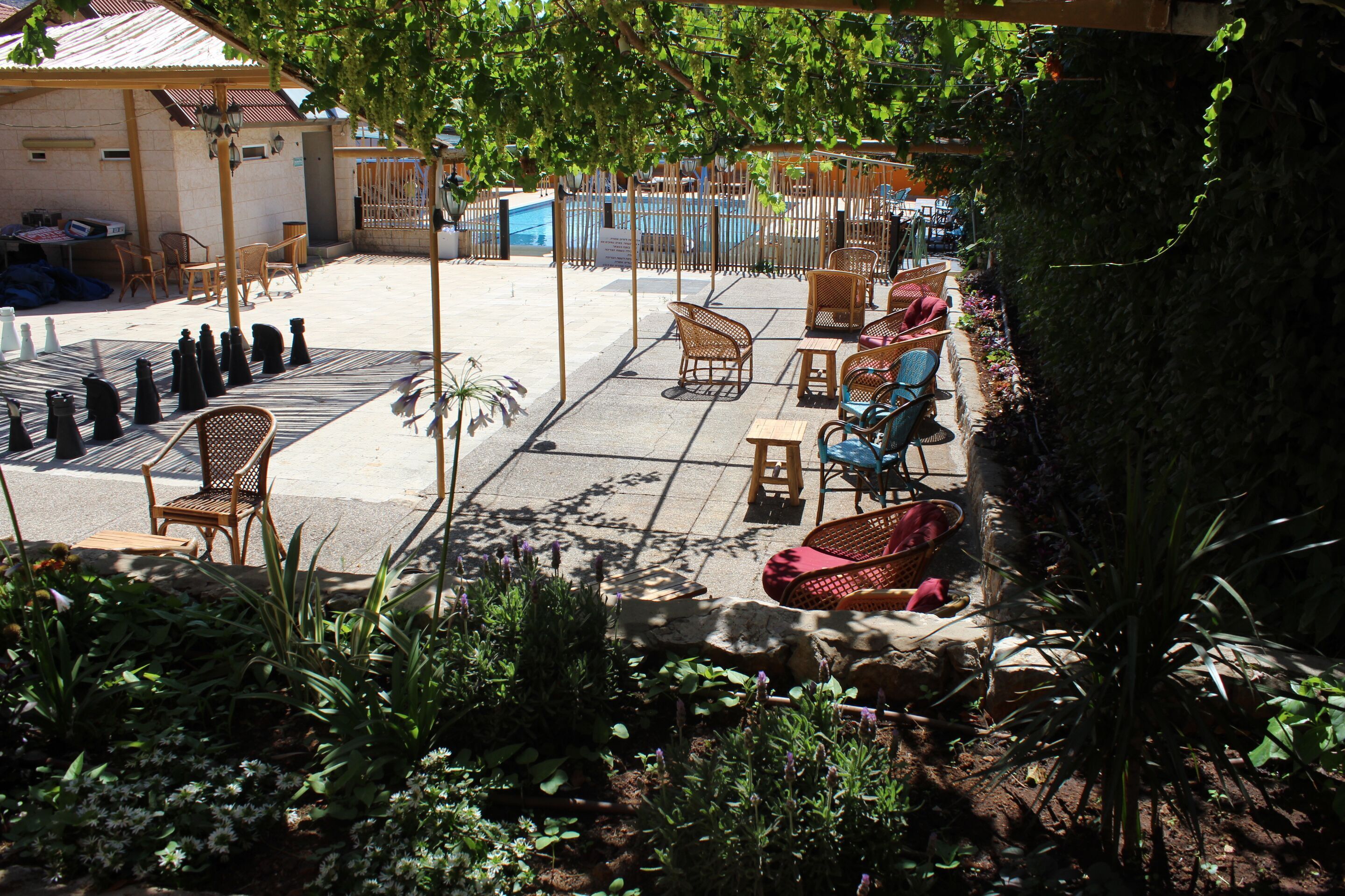 An outdoor patio area with wicker furniture, a pool, and a garden.