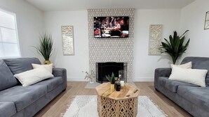 Een moderne woonkamer met twee grijze banken, een houten salontafel en een flatscreen televisie boven een open haard.