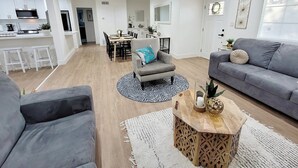Een moderne woonkamer met een grijze bank, een ronde salontafel, en een eethoek met een tafel en stoelen.