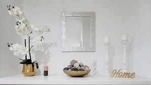 Een witte wastafel met gouden handgrepen, een spiegel, een schaal met decoratieve voorwerpen en een bordje met de tekst 'Home'.