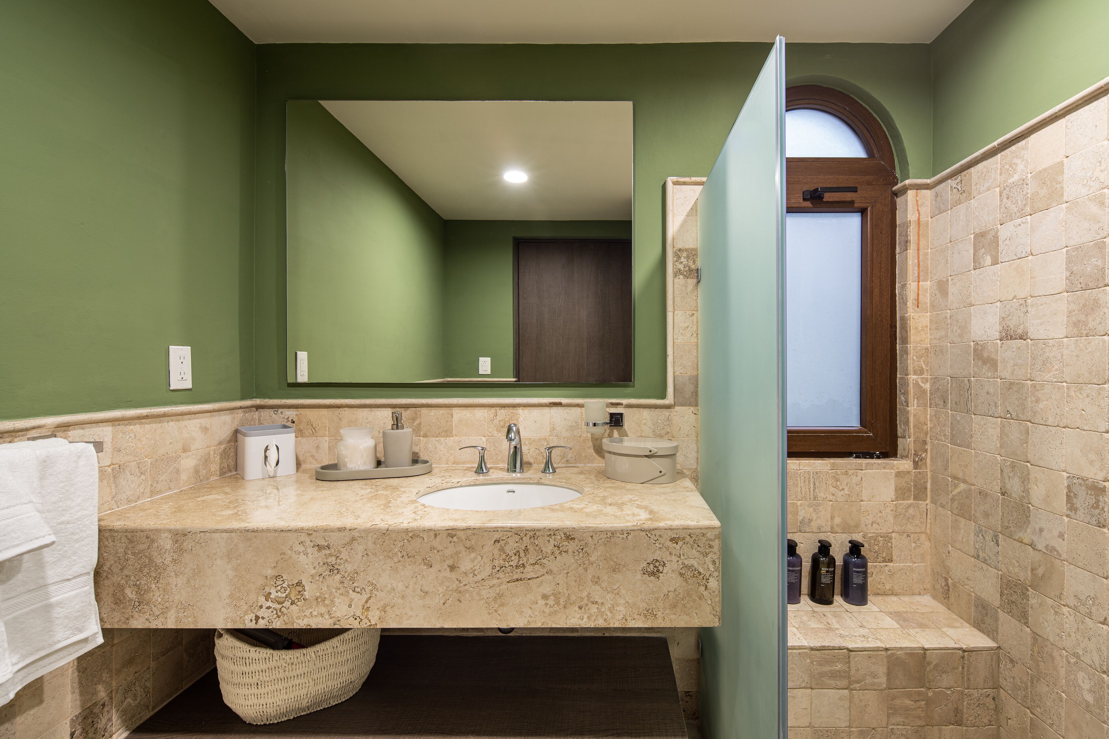 A bathroom with a marble sink, green walls, a large mirror, and a shower area.