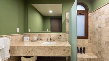 A bathroom with a marble sink, green walls, a large mirror, and a shower area.