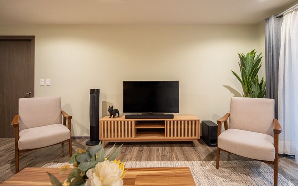 Una sala de estar moderna con un televisor de pantalla plana, dos sillones, una mesa de centro de madera y una planta en maceta.