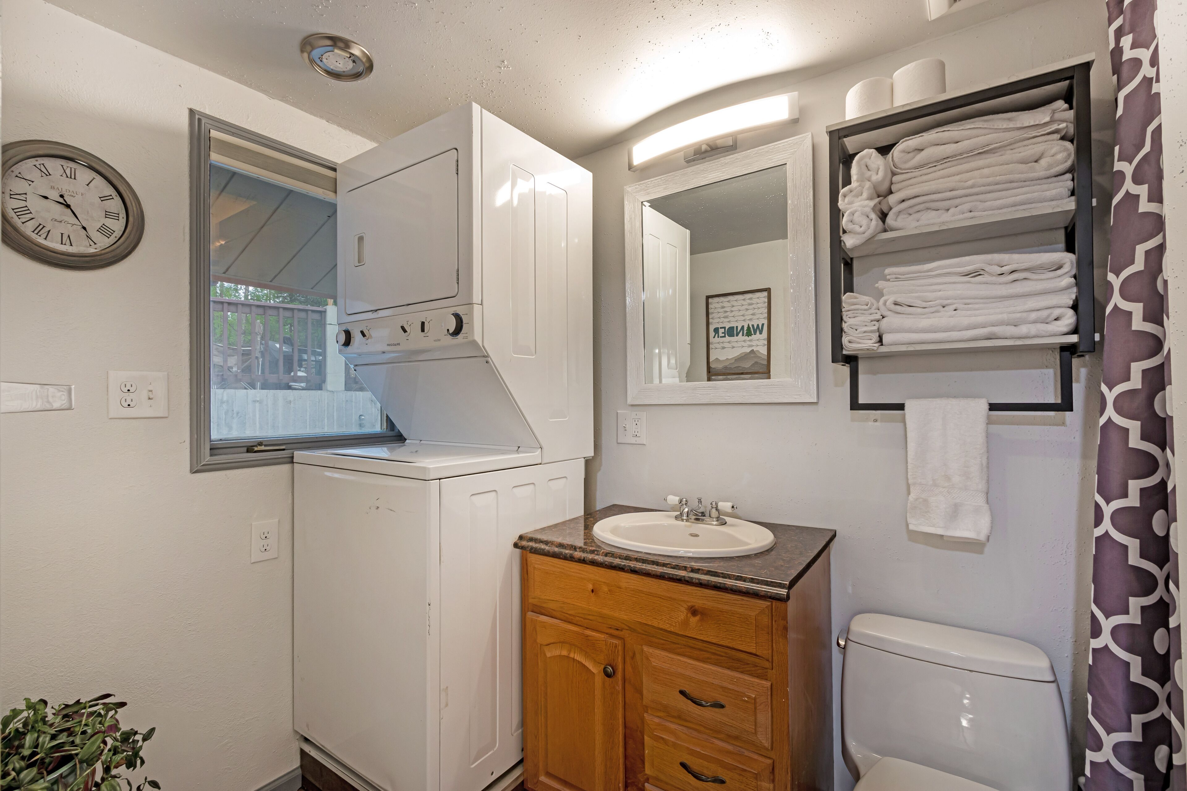 Une salle de bain avec des toilettes blanches, un lavabo doté d’un plan de travail en marbre, des meubles en bois, un miroir et un porte-serviettes avec des serviettes pliées.