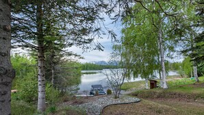 Una cabaña junto al lago con un muelle, rodeada de abedules y vistas a montañas distantes.