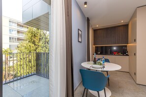 A modern apartment with a balcony, a dining area with a table and chairs, a kitchen with dark wood cabinets, and a view of a tree and building. - ICON H Lugano 309 Suite Micro-Living, Lugano, Switzerland (Lugano)