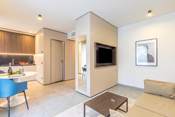 A modern living room with a flat-screen TV, a sofa, a coffee table, and a dining area with a table and chairs. - ICON H Lugano 309 Suite Micro-Living, Lugano, Switzerland (Lugano)