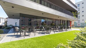A modern outdoor seating area with chairs and tables, surrounded by a well-maintained lawn and a building with large windows. - ICON H Lugano 204 Suite Micro-Living, Lugano, Switzerland (Lugano)