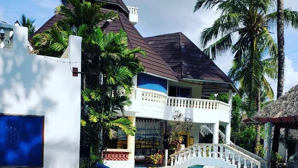 Un espace piscine avec une eau d’un bleu limpide, un bâtiment blanc doté d’un balcon et des palmiers.