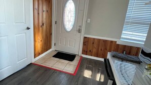 A hallway with a white door, a red exit sign, a black doormat, and a window with blinds.