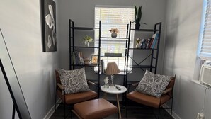 A cozy reading nook with two leather chairs, a small table, and a bookshelf filled with books and decorative items.