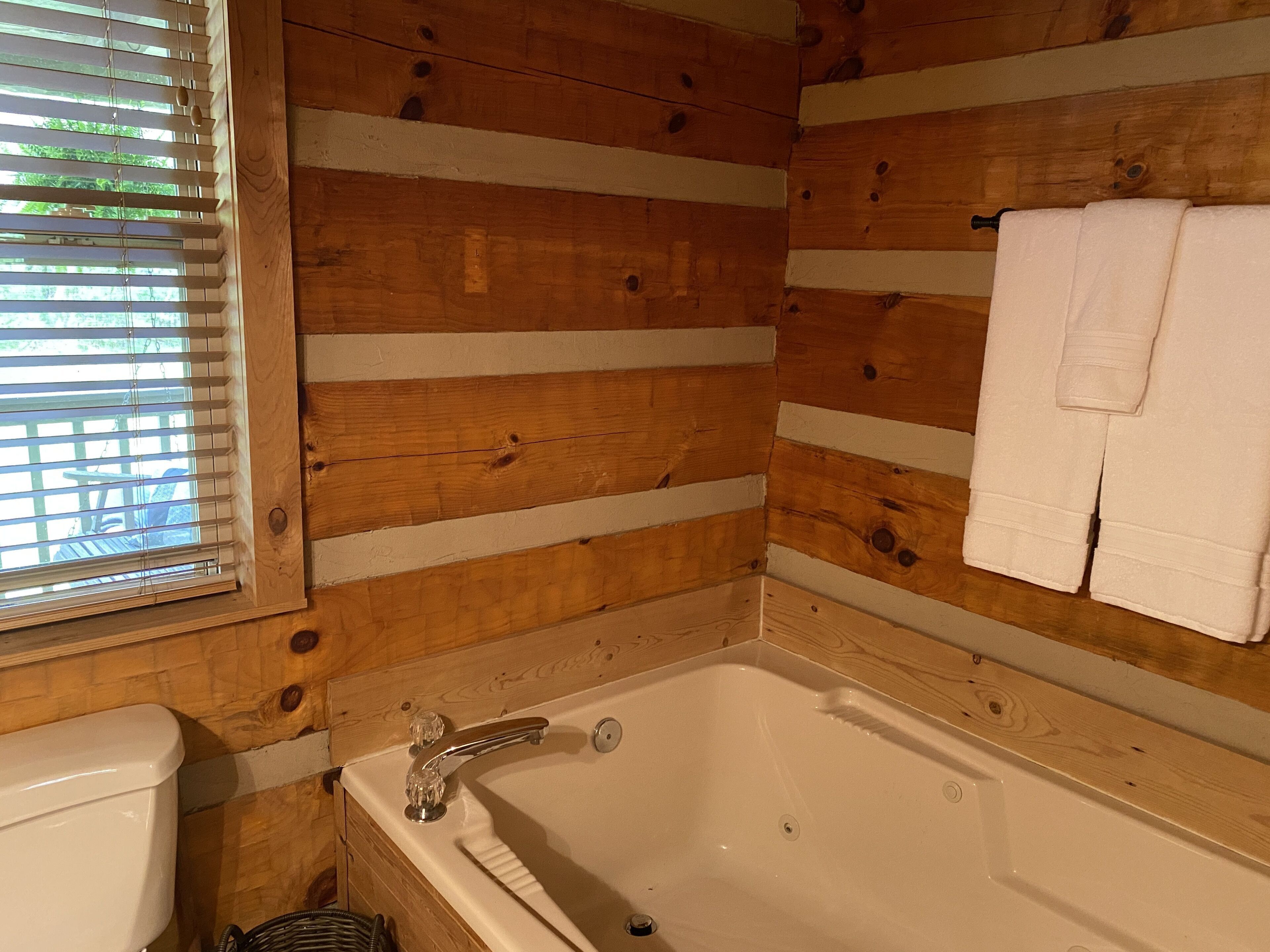 Ein Badezimmer einer Holzblockhütte mit Badewanne, Toilette und einem Fenster mit Jalousien.