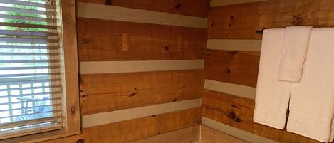 Ein Badezimmer einer Holzblockhütte mit Badewanne, Toilette und einem Fenster mit Jalousien.