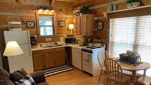 A cozy cabin-style kitchen with wooden cabinets, a refrigerator, a stove, and a dining area with a table and chairs. - Beautiful Authentic Log Cabin on Cosby Creek (Cosby)