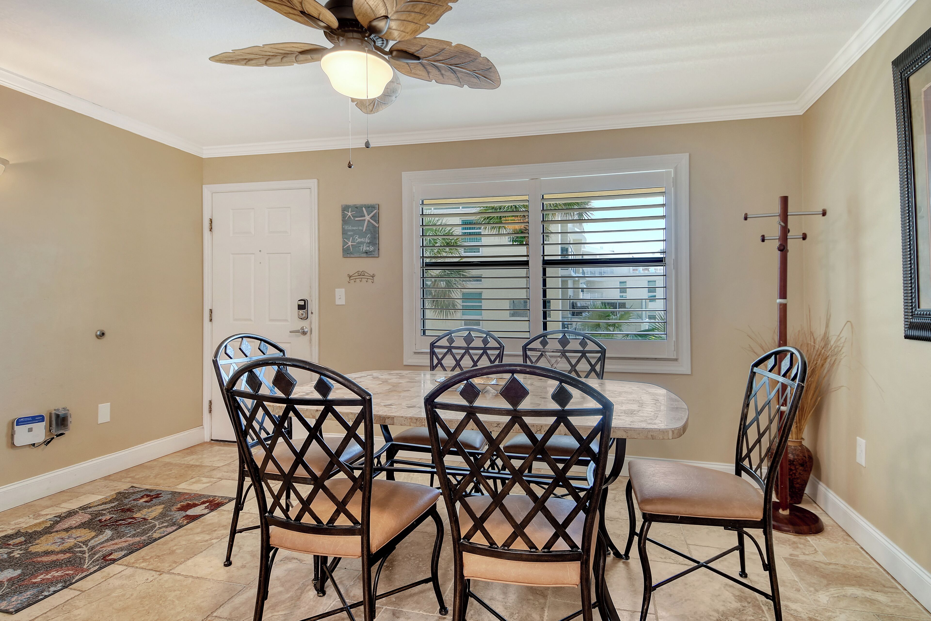 A dining area with a round table and six chairs, a ceiling fan, and a window with blinds.