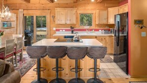 A modern kitchen with wooden cabinetry, a central island with bar stools, and a refrigerator. - Timber Cabin in the woods (Cle Elum)