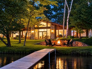 Um imóvel à beira do lago com um cais, área de estar externa e lareira de pedra.