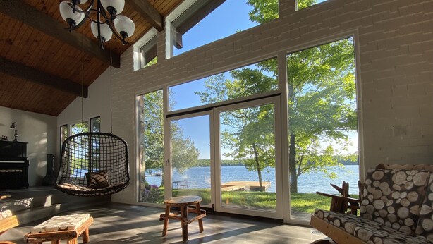 Ein geräumiges Wohnzimmer mit großem Fenster mit Seeblick, Holzmöbeln und einem Hängesessel.