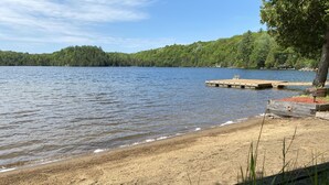 Ein Strand am See mit einer Holzsteganlage und einem bewaldeten Hügel im Hintergrund.