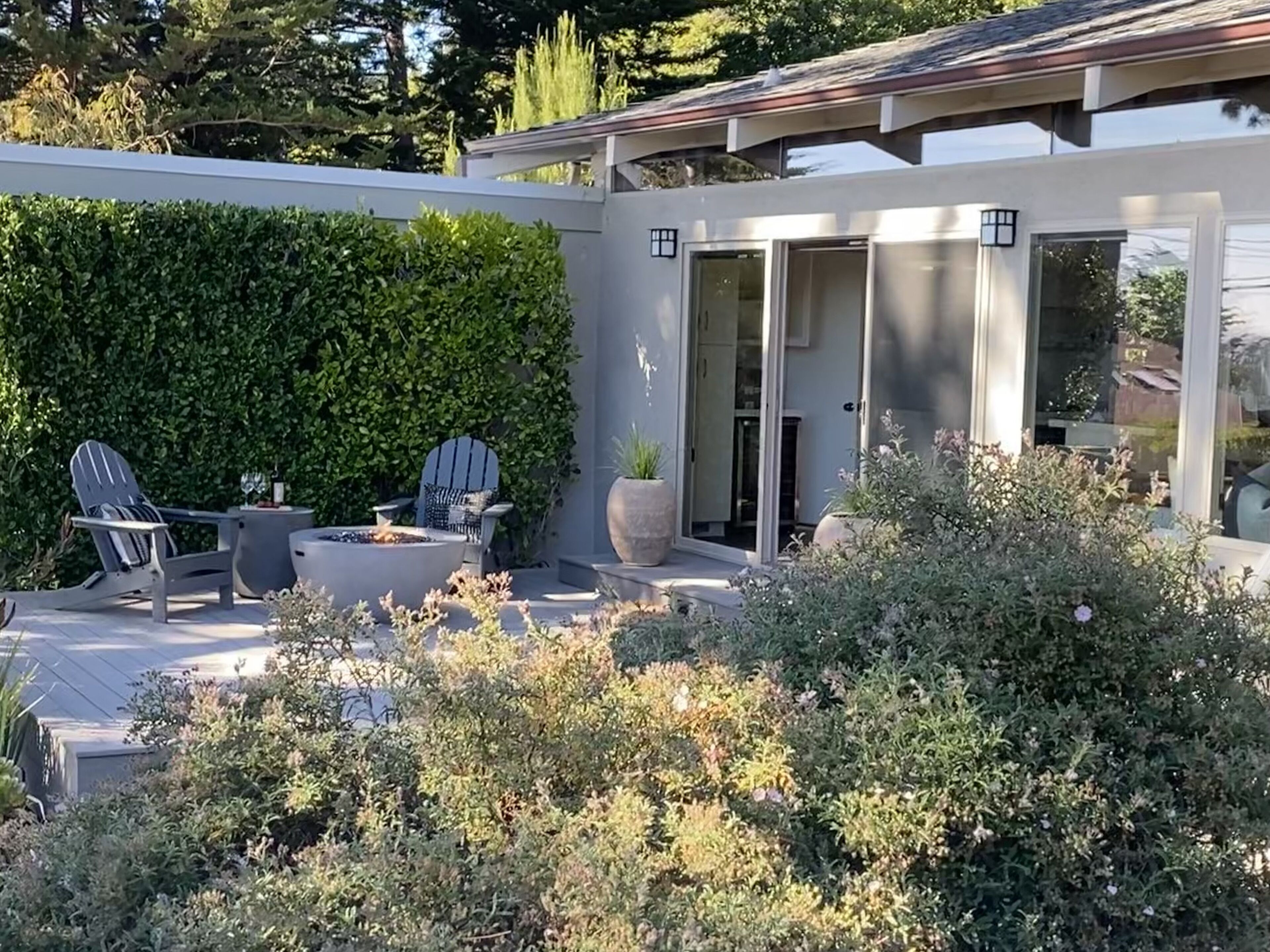 A modern outdoor patio with a fire pit, two Adirondack chairs, and a large potted plant.