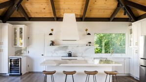 A modern kitchen with white cabinets, a marble countertop, and a large window overlooking greenery. - “Pacific Horizons” hot tub, ocean views, Gateway to Big Sur (Carmel-by-the-Sea)