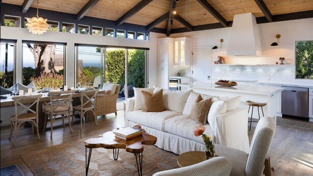 A spacious living area with a high ceiling, large windows, a white sofa, and a kitchen with white cabinets. - “Pacific Horizons” hot tub, ocean views, Gateway to Big Sur (Carmel-by-the-Sea)