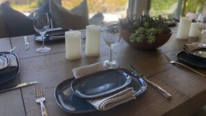 A dining table set with plates, glasses, cutlery, candles, and a potted plant. - “Pacific Horizons” hot tub, ocean views, Gateway to Big Sur (Carmel-by-the-Sea)