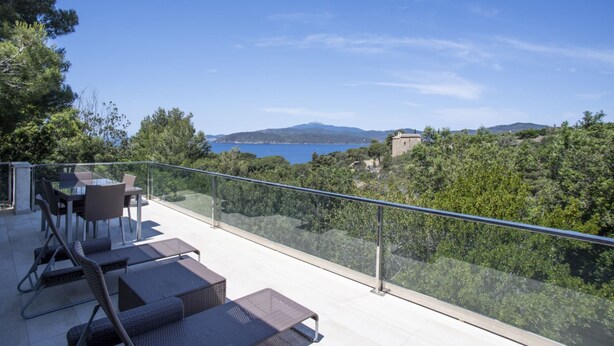 Un balcon doté de meubles en osier, offrant une vue panoramique sur la mer et les collines.