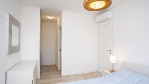 Une chambre à coucher comprenant un lit, une table de chevet, une lampe, un appareil de climatisation et une porte donnant sur une autre pièce.