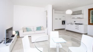 Un salon moderne et minimaliste, avec un canapé blanc, une table basse en verre et un téléviseur posé sur une console blanche.