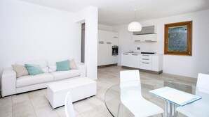 Un salon moderne avec un canapé blanc, une table à manger en verre et une cuisine en arrière-plan.