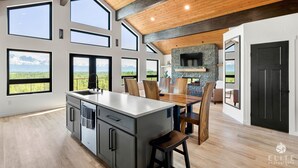 Une cuisine spacieuse dotée d’un grand îlot central, d’une cheminée en pierre et de nombreuses grandes fenêtres offrant une vue sur les montagnes.