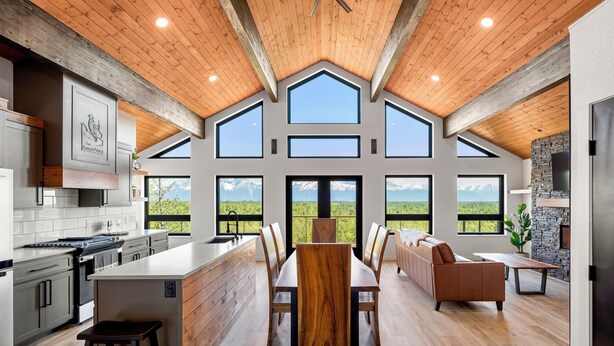 Une cuisine spacieuse dotée d’un grand îlot central, un coin repas avec une table et des chaises en bois, et un salon avec un canapé et une cheminée.