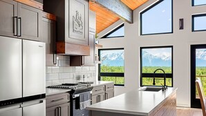 Une cuisine moderne dotée d’appareils électroménagers en acier inoxydable, d’un grand îlot central et offrant une vue sur les montagnes par les fenêtres.