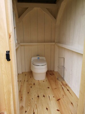 Simple, compact room with a toilet, wooden floor, and metal storage.